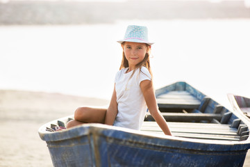 Young girl sitting in old wooden boat on the beach in Dubai