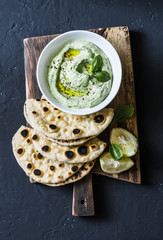 Avocado, Greek yogurt dip and whole grain flatbreads on wooden rustic cutting board on dark...