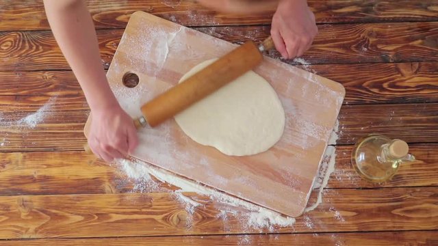 Woman's hands rolling dough on wooden board, top view video