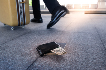 Leather purse with a money and passport lying on the sidewalk and feet of outgoing man