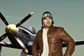 Portrait of a vintage pilot with leather cap, scarf and aviator glasses in front of a historic airplane - Portrait of a man in historical pilot clothing - obrazy, fototapety, plakaty