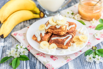 Cottage cheese pancakes in the form of cubes with banana, yogurt, honey and cherry blossom flowers on grey wooden background. Healthy breakfast food.