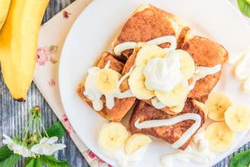 Cottage cheese pancakes in the form of cubes with banana, yogurt, honey and cherry blossom flowers on grey wooden background. Healthy breakfast food.