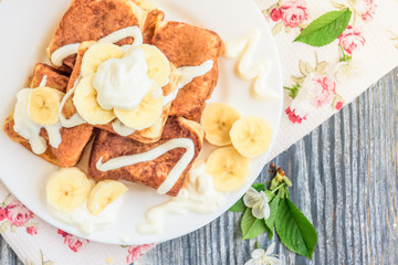 Cottage cheese pancakes in the form of cubes with banana, yogurt, honey and cherry blossom flowers on grey wooden background. Healthy breakfast food.