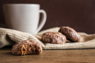Glazed, chocolate russian gingerbreads or small spice cakes with mug of beverage on the dark, wooden vintage table. Enjoying coffee and sweets. Drink and snack concept.