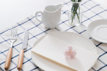 Table setting with dishes, cutlery and flowers on white background