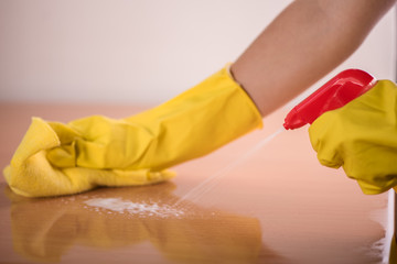 detail of yellow rubber hands spraying cleaning table 
