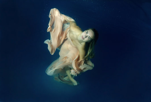 Young beautiful woman in a long dress underwater