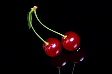 Symmetric reflection of red sour cherry on a black reflective surface