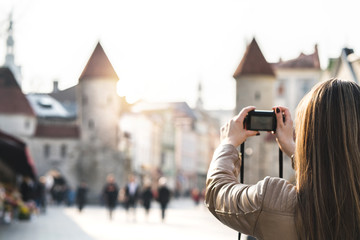 Woman in Tallinn taking photo of Viru Gate. Tourist on vacation taking picture of landmark in Estonia. People walking in popular street. Back view of girl with camera. - obrazy, fototapety, plakaty