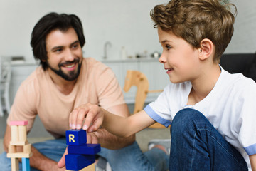 selective focus of father and son playing with wooden blocks together at home