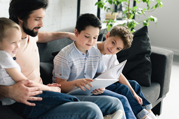 side view of father and sons reading book together at home