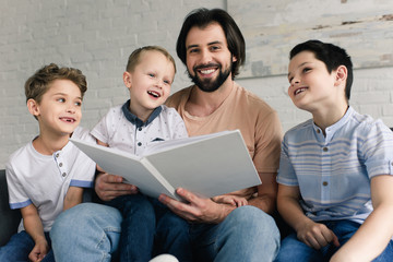 portrait of smiling father and sons reading book together at home
