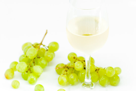 glass with white dry wine and white grapes on white background