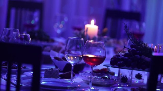 Banquet table in a restaurant with glasses and a candle, a glass with red and white wine on a banquet table on a background of a burning candle, a decorative wax candle in the pendant on a table