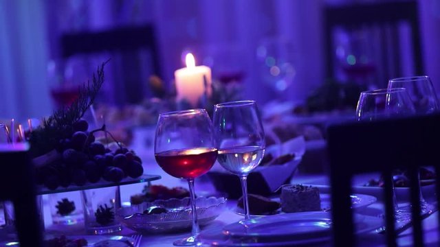 Banquet table in a restaurant with glasses and a candle, a glass with red and white wine on a banquet table on a background of a burning candle, a decorative wax candle in the pendant on a table