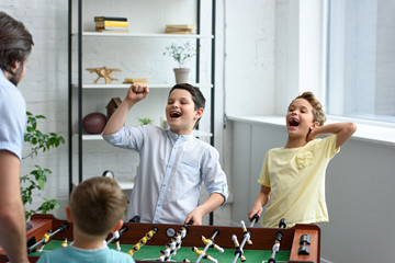 father and happy little sons playing table football together at home