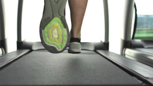 Slow motion shot of a sporty adult woman's legs running on a treadmill in a gym
