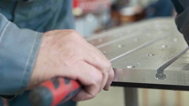 Male hands chamfering removing burrs on metal detail for manufacturing cnc machinery with a scraper