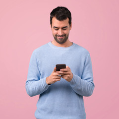 Man with blue sweater using mobile phone on pink background