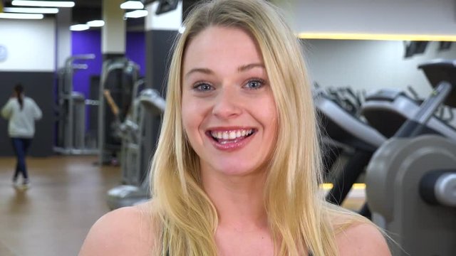 A young beautiful woman talks to the camera in a gym - face closeup