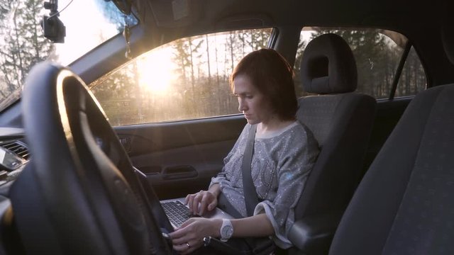 Woman businesswoman working with laptop in car salon. Girl with laptop sitting in car.