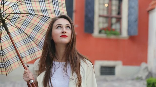 handsome cheerful woman looking up the sky for checking if the rain stop smiling and close her umbrella enjoying sunny weather fashion casual clothes walking alone in the city traveling brunette girl