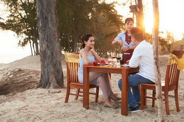 Romantic date at sunset: affectionate young couple sitting at table of beach restaurant and...