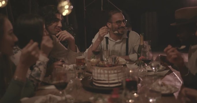 Multi-ethnic friends eating gourmet birthday cake at rustic dinner party
