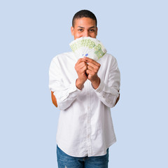 Young african american man with white shirt taking a lot of money on isolated blue background