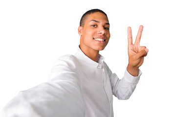 Young african american man  taking a selfie with the mobile and smiling and showing victory sign on isolated white background