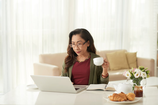 Senior woman drinking coffee and using laptop for online shopping