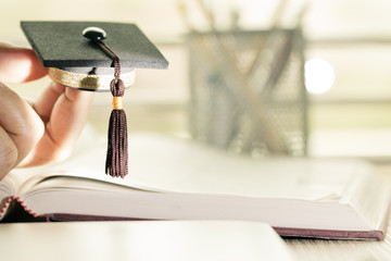 Student hands holding Graduation cap on  Books document in Library room of campus and university. Concept of Graduate abroad international Educational and Back to School.