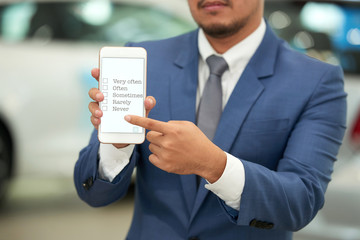 Close-up shot of bearded automobile dealer wearing elegant suit showing smartphone screen with...
