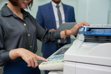 Close-up shot of smiling office assistant using multi-function printer in order to make copy of...