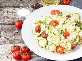fresh diet vegetable salad with couscous, tomatoes, cucumbers, parsley, dark rustic wooden table, side view