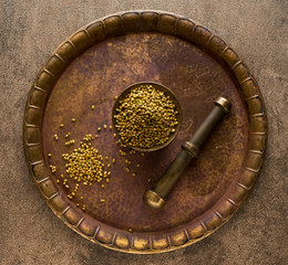 Dried coriander seeds in a mortar on a metal tray, top view