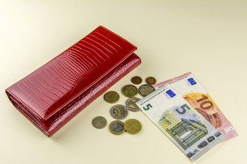 Red woman wallet. Banknotes ten and five euros. A few coins. Beige background.