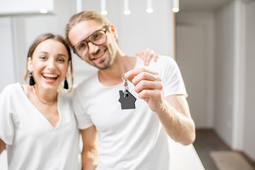 Portrait of a young and happy couple dressed in white t-shirts holding home keys indoors