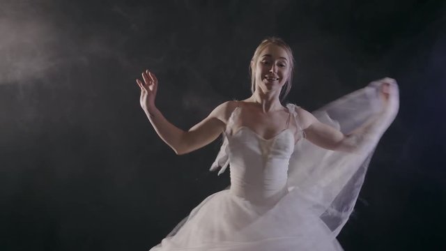 graceful sensual ballerina in white tutu dress dancing elements of classical or modern ballet in the dark with light and smoke on the black background, slow motion