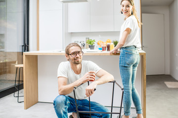 Young lovely couple doing house chores assembling a new chair at the kitchen of the modern apartment