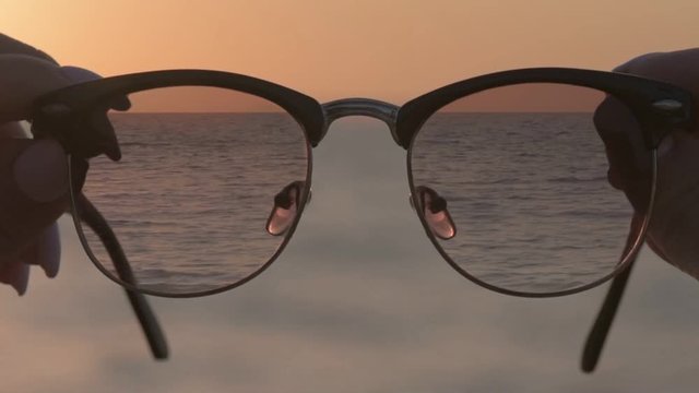 Cinemagraph - Woman's hands hold eyewear, a background of blue seawater. Motion Photo.