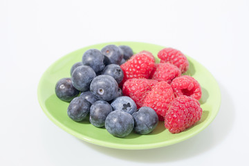 Fruit composition, blueberries and raspberries on a green plated isolated in a white background