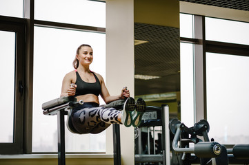 Fototapeta premium Portrait of sexy muscular girl wearing sportswear doing exercise on the bar raises his legs up, exercises on the press in the gym. Sport concept.