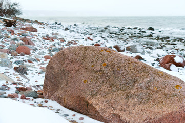 Huge boulder on the beach. Rocky sea coast. Sea shore in winter the rocks under the snow.