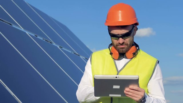 Male engineer is looking at a solar panel and noting something in his computer