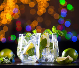 Closeup of mojito cocktails on a bar lights background. Ingredients and utensils.