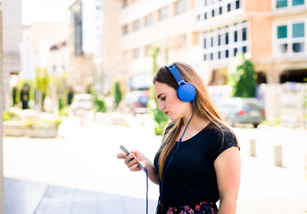 YOUNG WOMAN LISTENING MUSIC IN HEADPHONES IN THE CITY