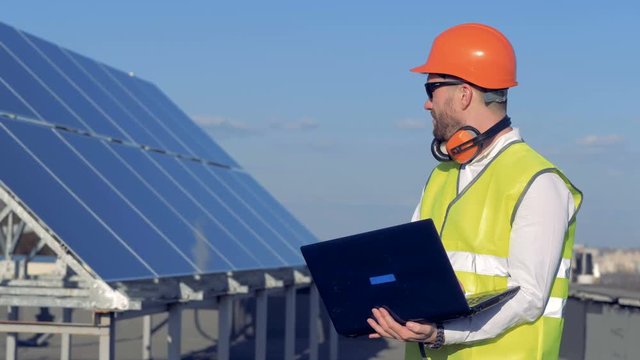 Solar battery and a male constructor working with his laptop nearby. Ecology Power Conservation Concept.