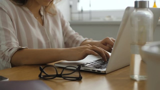 In this footage you can see young professional caucasian female working with laptop computer in home office or small agency studio. Her hands typing on keyboard while writing a text or letter.